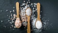 Different types of salt. Sea, himalayan and kitchen salt. Top view on three wooden spoons on black background