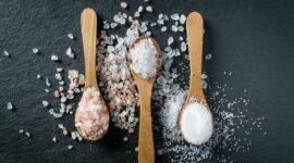 Different types of salt. Sea, himalayan and kitchen salt. Top view on three wooden spoons on black background