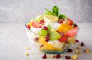 Fresh fruit salad with yogurt and walnuts in glass bowl on stone background. Healthy Eating. Selective focus.