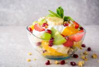 Fresh fruit salad with yogurt and walnuts in glass bowl on stone background. Healthy Eating. Selective focus.