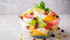 Fresh fruit salad with yogurt and walnuts in glass bowl on stone background. Healthy Eating. Selective focus.