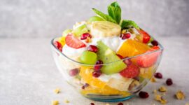 Fresh fruit salad with yogurt and walnuts in glass bowl on stone background. Healthy Eating. Selective focus.