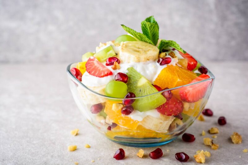 Fresh fruit salad with yogurt and walnuts in glass bowl on stone background. Healthy Eating. Selective focus.