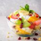 Fresh fruit salad with yogurt and walnuts in glass bowl on stone background. Healthy Eating. Selective focus.